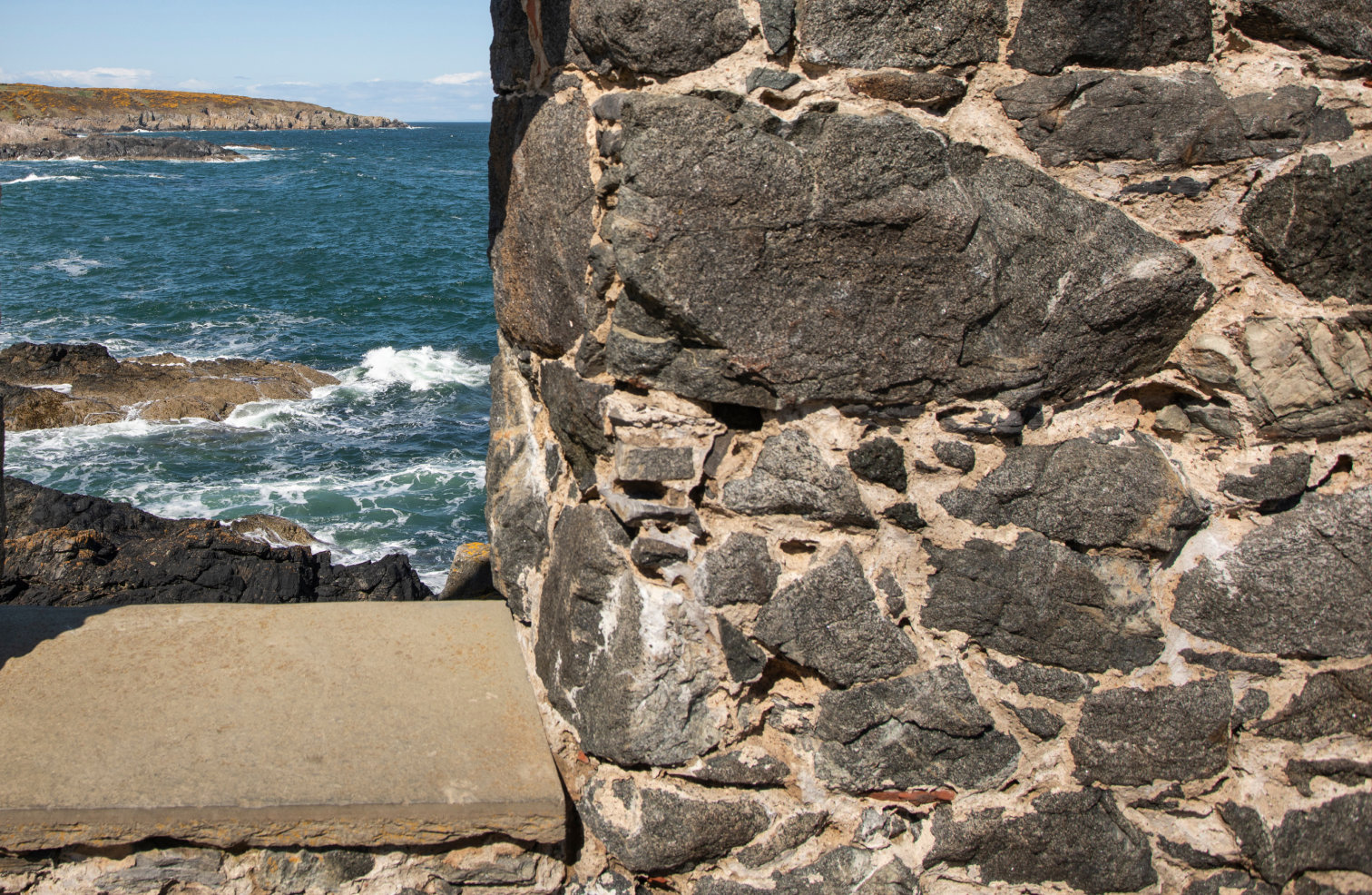 Close up view of the rocks forming a building and the ocean in the background.