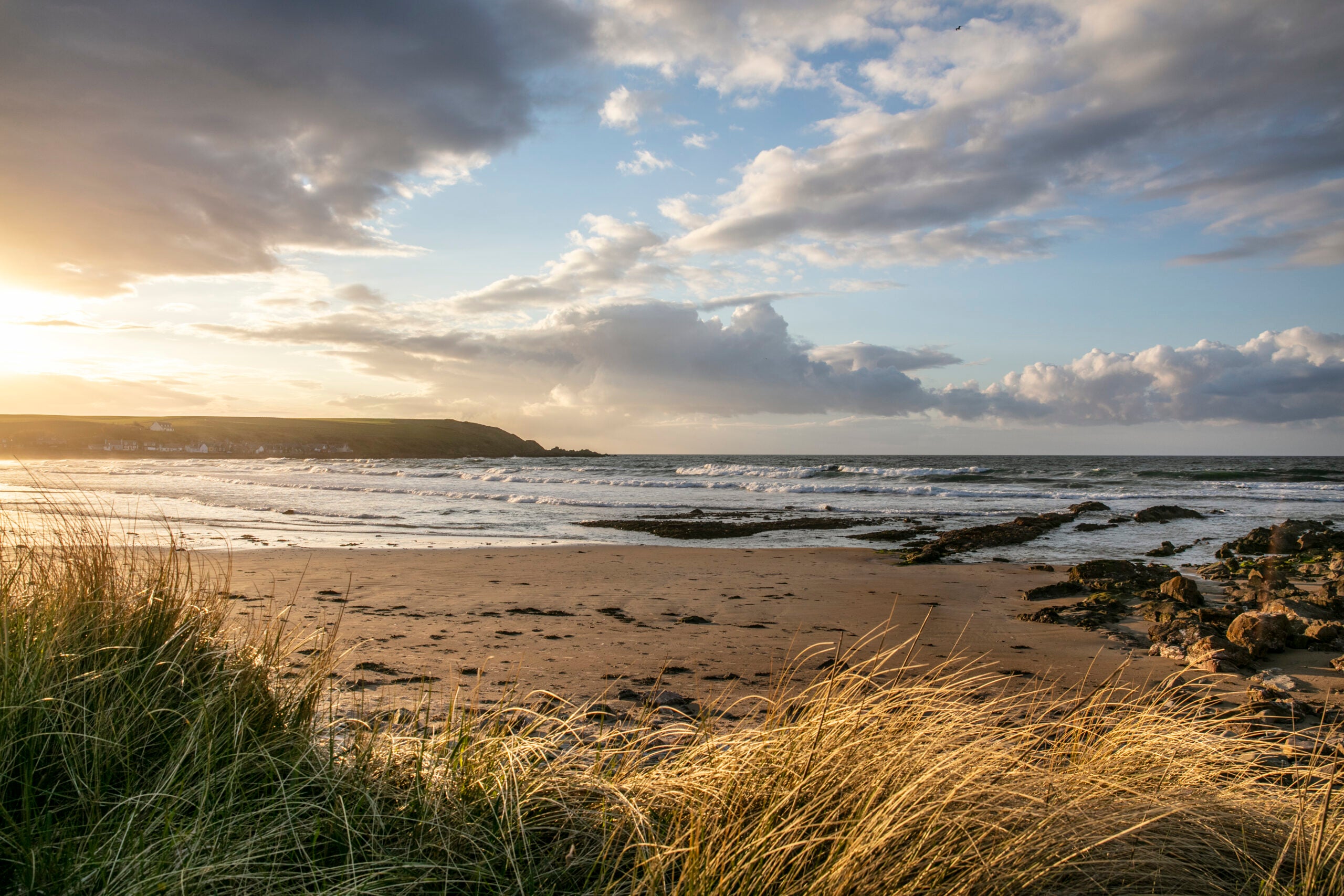 Sunset shot of the clouds, ocean, rocks and grass.