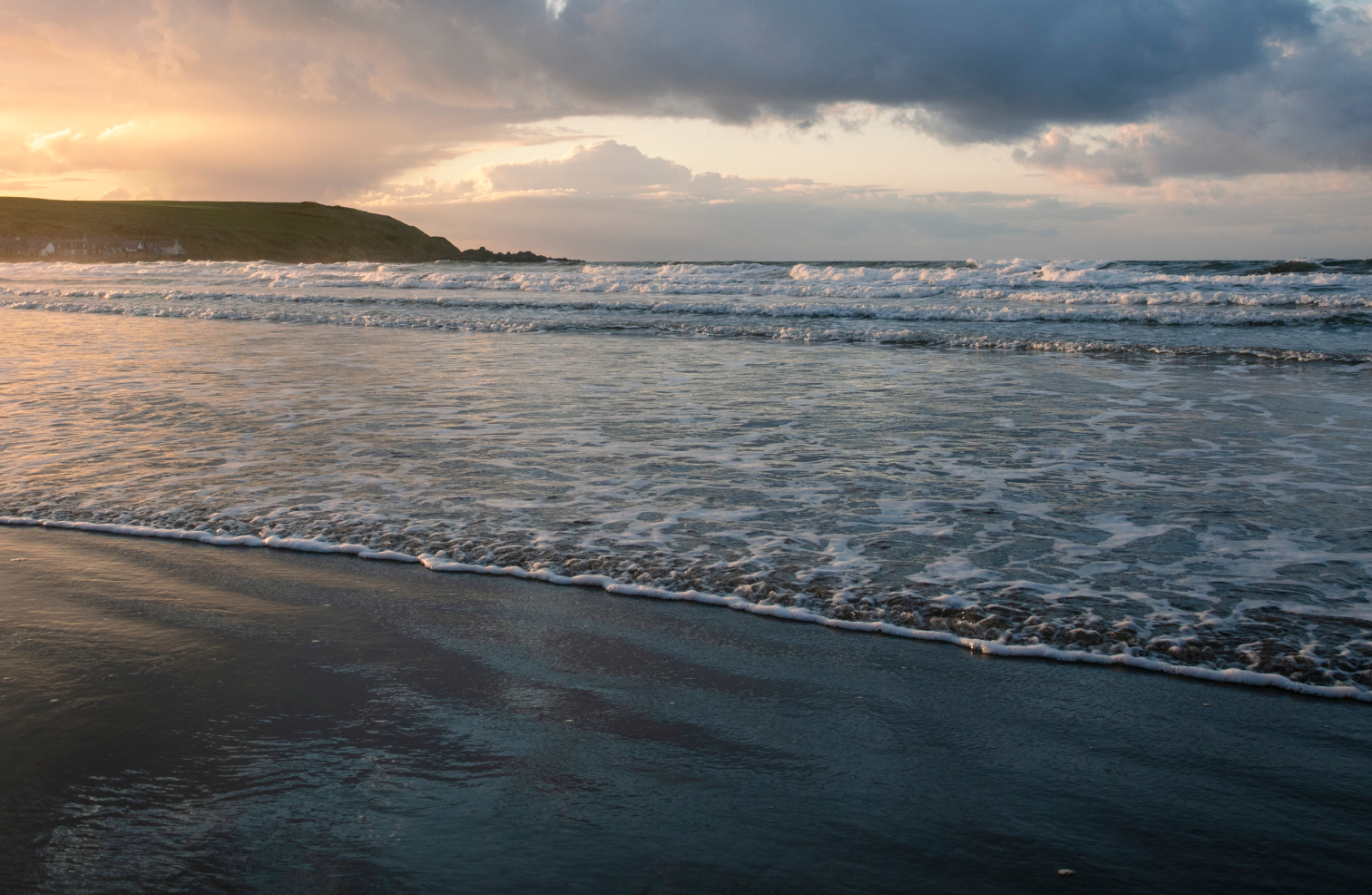 Close up of the wet sand and waves crashing onto the shore at sunset.