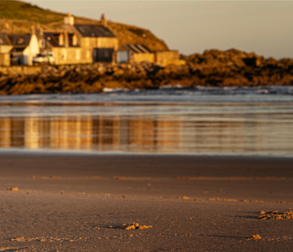 The sand and water at sunset and the distillery in the background.